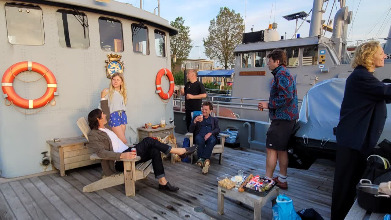 Een groep vrienden ontspant samen op het houten dek van een oud marineschip in de avondzon