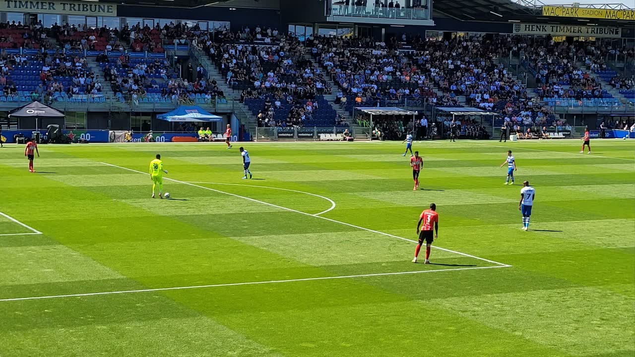 Een voetbalwedstrijd in een zonovergoten stadion met volle tribunes